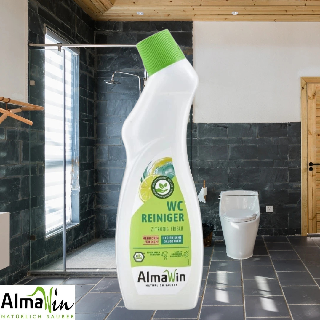 AlmaWin WC cleaner (lemon fresh) bottle with a green cap superimposed over a modern tiled bathroom featuring a glass shower and a white toilet; AlmaWin logo in the bottom-left corner.